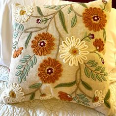 a close up of a pillow on a bed with white linens and orange flowers