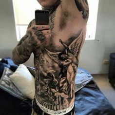 a man with tattoos on his back holding a cell phone in his hand and taking a selfie