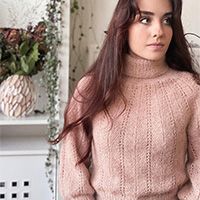 a woman wearing a pink sweater standing in front of a shelf with flowers on it