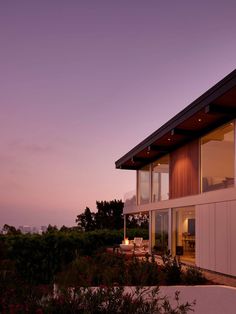 an exterior view of a modern home at dusk with the ocean in the back ground