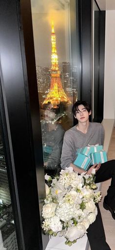 a person sitting on a ledge with flowers and gifts in front of the eiffel tower