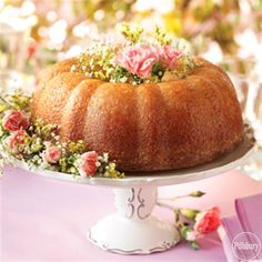 a bundt cake with flowers on top is sitting on a white platter next to pink napkins