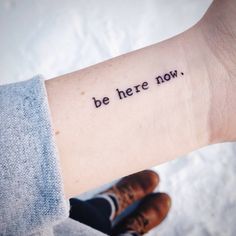 a person with a wrist tattoo that says, be here now