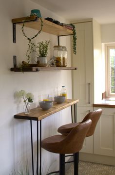 two brown chairs sitting in front of a wooden shelf with bowls and cups on it