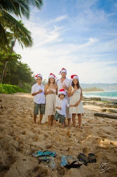 a group of people standing on top of a sandy beach next to the ocean wearing santa hats