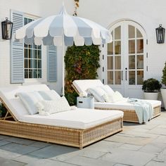 two wicker chaise lounges with white pillows and an umbrella on the patio