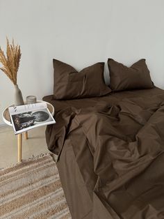 a bed with brown sheets and pillows in a white room next to a side table