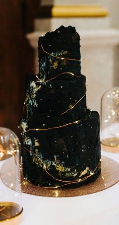 a three tiered black cake on top of a table next to candles and other decorations