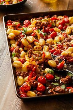 a casserole dish with pasta, tomatoes and meat in it on a wooden table