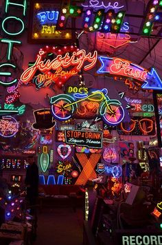 many neon signs are lit up on the wall in this shop's storefront