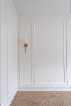 an empty room with white paneling and a gold lamp on the wall in front of it