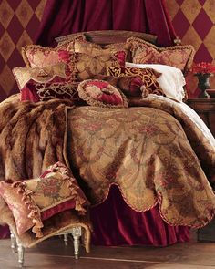 a bed with red and gold comforters, pillows and blankets on top of it