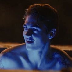 a man with blue paint on his face and chest in a bathtub looking at the camera