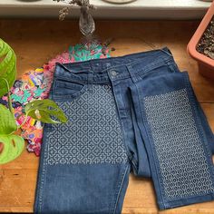 two pairs of blue jeans sitting on top of a wooden floor next to a potted plant