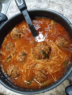 a pot filled with meatballs and noodles on top of a counter next to a spatula