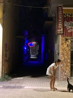 a woman standing on the sidewalk next to a black dog