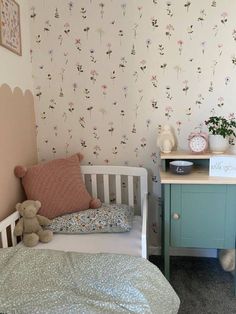 a small child's bedroom with floral wallpaper and bedding, including a teddy bear