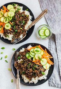 two plates with rice, meat and cucumbers next to a glass of water