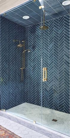 a walk in shower sitting next to a blue tiled wall with gold fixtures on it