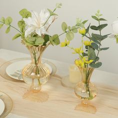 three vases filled with flowers sitting on top of a wooden table next to plates