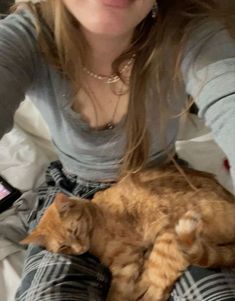 a woman sitting on top of a bed holding an orange and white cat in her lap