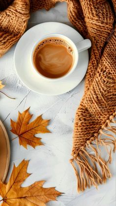 a cup of coffee on top of a saucer next to autumn leaves and a scarf