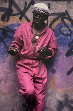 a man in pink jumpsuits standing next to a wall with graffiti on it