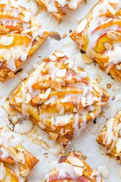 several pieces of dessert sitting on top of a white tray covered in icing and almonds