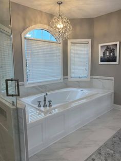 a large white bath tub sitting in a bathroom next to two windows with blinds on them