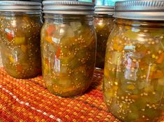 four jars filled with pickles sitting on top of a red and orange table cloth