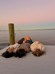 two young women laying on the end of a boat in front of a body of water