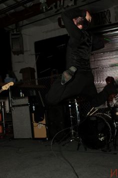 a man jumping up in the air with his legs spread out while playing an electric guitar