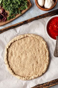 an uncooked pizza crust sitting on top of a table next to other ingredients