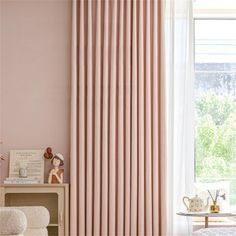 a living room with pink walls and white curtains on the window sill, in front of a chair