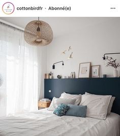 a bed with white linens and blue headboard next to a window in a bedroom