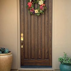 a front door with a wreath on it and two potted plants next to it