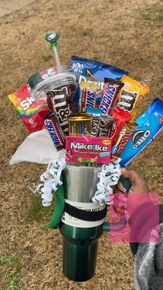 a person holding a cup filled with candy and candies on top of a grass covered field