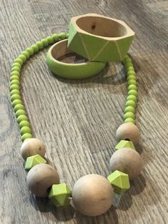 a wooden bead necklace with green beads on a wood table next to a cup