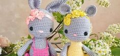 two crocheted stuffed animals sitting next to each other on a table with flowers