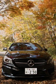 a black car parked on the side of a road in front of trees with leaves