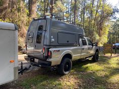 a truck with a camper attached to it parked in the woods next to a trailer