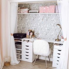 a white desk sitting under a window next to a wallpaper covered in pink flowers