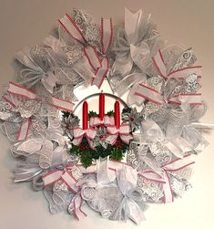 a christmas wreath with two red candles on the front and white ribbons hanging from it