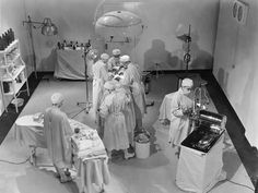 black and white photograph of doctors in an operating room with medical equipment on the floor