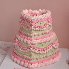 a three tiered cake with pink and green icing on the top, sitting on a table