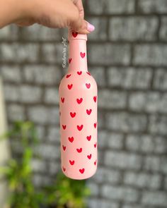 a hand holding a pink bottle with red hearts on it and a brick wall in the background