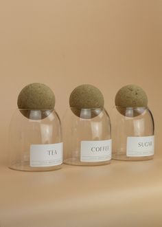 three glass jars with labels on them sitting on a table next to each other in front of a beige background