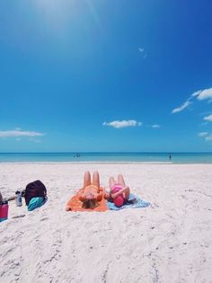 two people are laying on the beach with their feet in the sand and one person is lying down