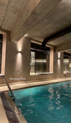 an indoor swimming pool with blue water and lights on the side of it, in front of a concrete building