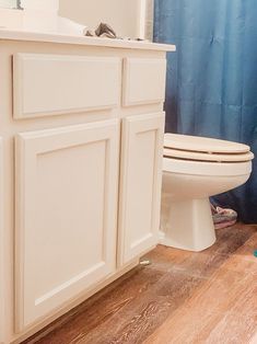 a white toilet sitting in a bathroom next to a blue shower curtain and wooden floors